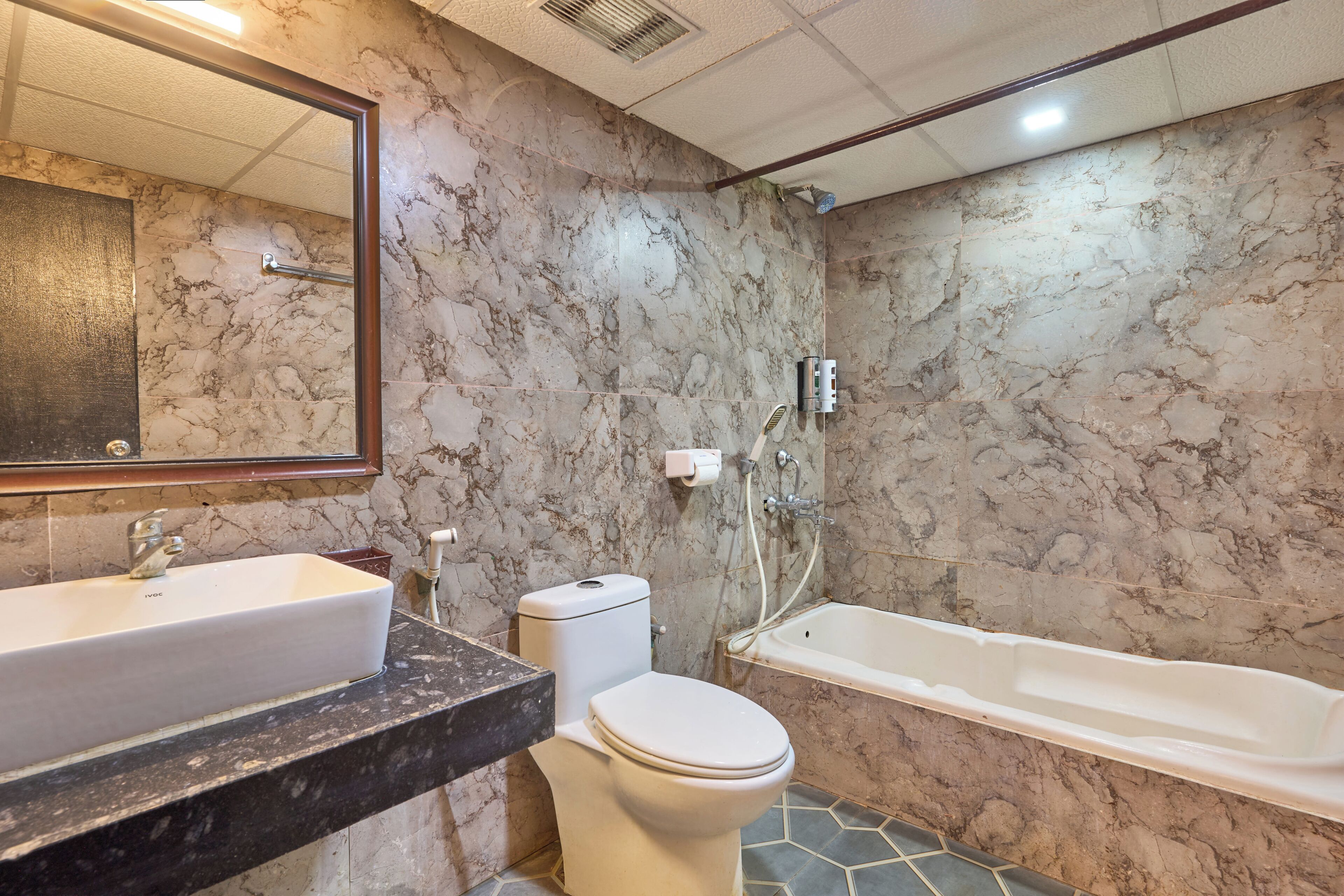 A bathroom with a marble wall, a sink, a toilet, and a bathtub.
