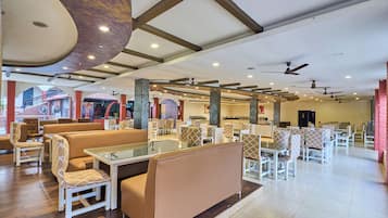 A spacious indoor area with multiple seating arrangements, including sofas and tables, and a ceiling with exposed beams and recessed lighting.