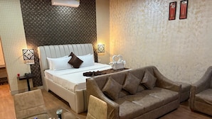 Une chambre d’hôtel avec un lit, un canapé, une table en verre avec des bouteilles d’eau et un mur recouvert d’un papier peint à motifs.