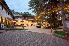 Ein Innenhof mit Pflasterweg, überdachter Sitzgelegenheit und einem Gebäude mit mehreren Fenstern und Balkonen.