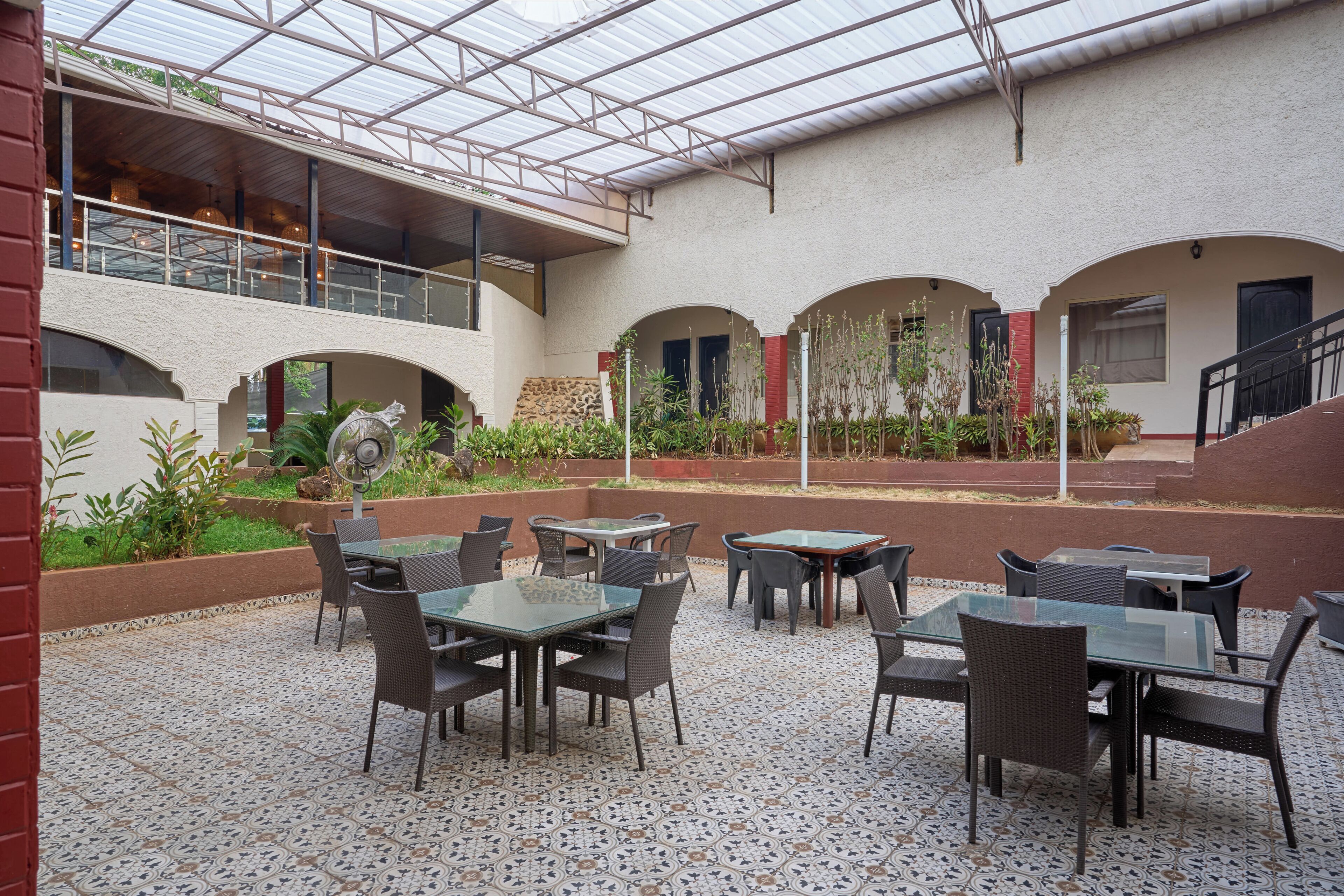 Un patio techado al aire libre con mesas y sillas, techo de vidrio y vista al interior del edificio.