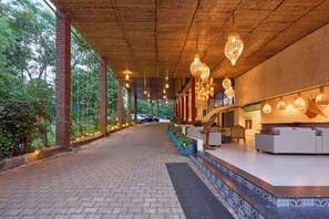 A covered walkway with brick pillars, hanging lights, and a reception area with seating. - Elim Resorts (Bengaluru)