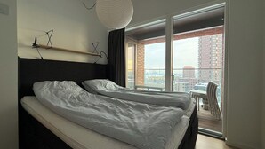 Een moderne hotelkamer met twee bedden, een kleine tafel en uitzicht op de stad door grote ramen.