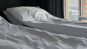Een moderne slaapkamer met een groot bed, een hoofdbord, een hanglamp en uitzicht op de stad door een raam.