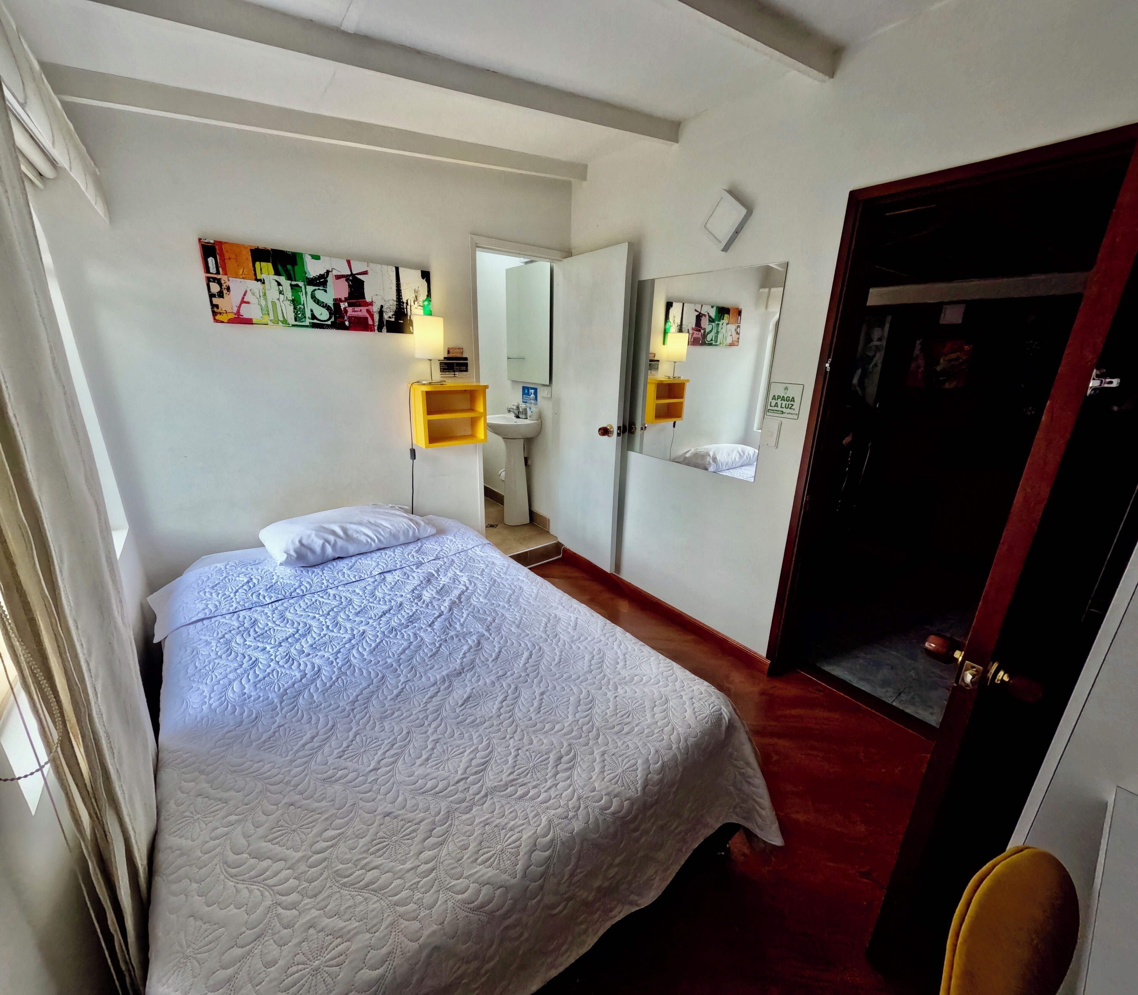 A hotel room with a bed, a mirror, a sink, and a door.