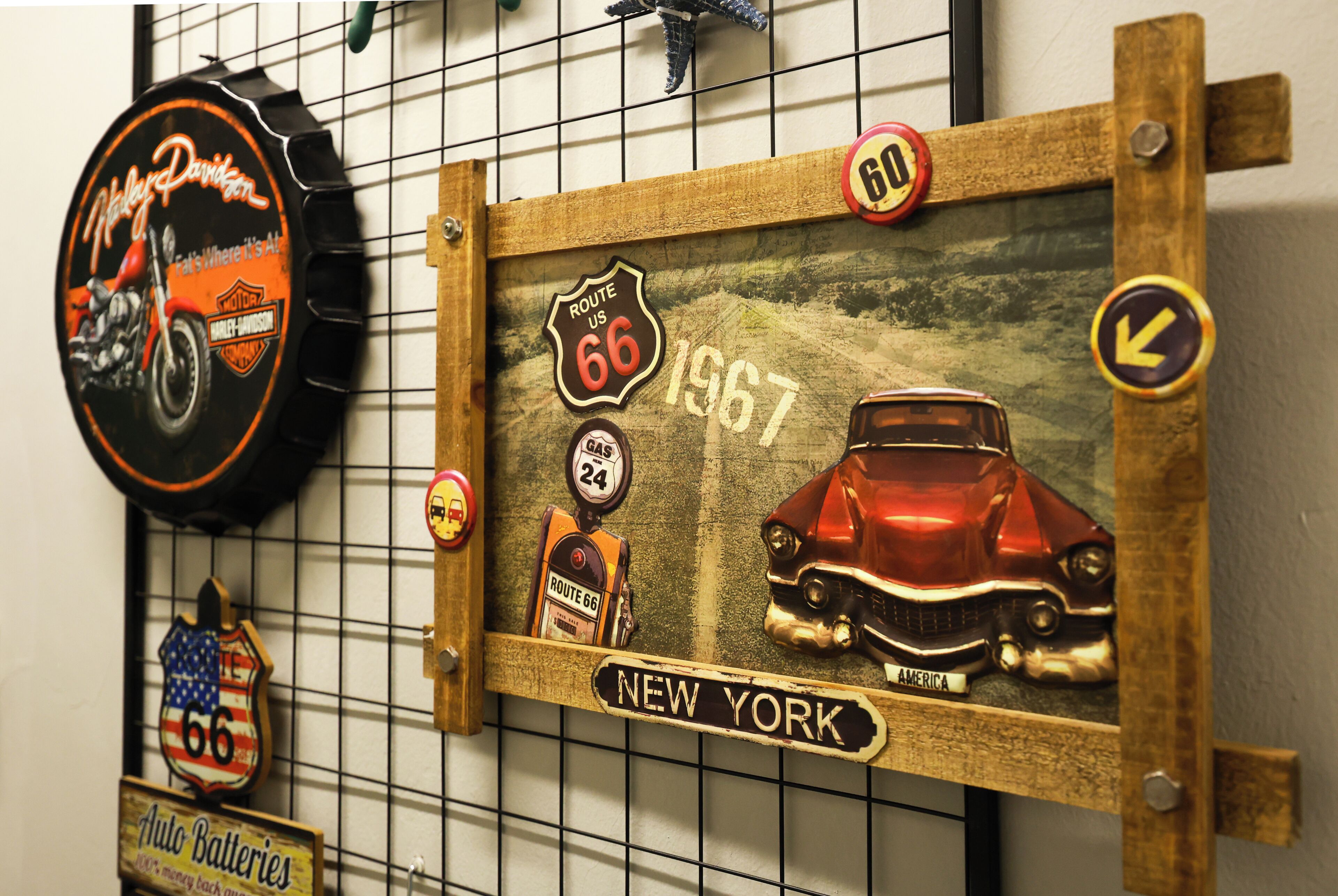 Una pared con diversas decoraciones de temática vintage, incluyendo señales de Route 66, un letrero de motocicleta Harley-Davidson y un coche antiguo.