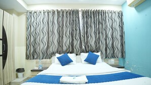 Une chambre d’hôtel avec un lit, des rideaux, une table de chevet et un climatiseur fixé au mur.