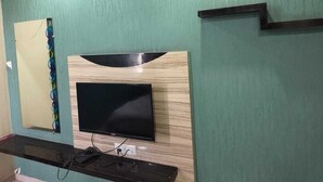 Un salon moderne avec un téléviseur à écran plat fixé sur un mur recouvert de panneaux en bois, une étagère intégrée en dessous et un miroir décoratif sur le côté gauche.