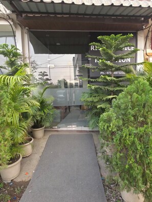Una entrada de edificio con puerta de cristal, rodeada de plantas en macetas.