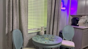 A room with a round table, two chairs, a window with blinds, curtains, a neon sign, a kitchen area, and a ceiling with a textured finish. - Stay Where You Play at Paradise Lakes! Sleeps up to 4! (Lutz)