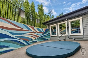 Un área de piscina con un mural colorido, un trampolín y una casa al fondo.