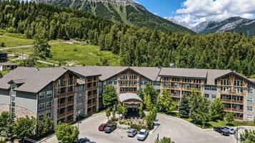 A multi-story hotel with a parking lot, surrounded by forested hills and mountains.