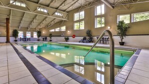 Una piscina interna con acqua cristallina, circondata da pavimentazione piastrellata e ampie finestre.