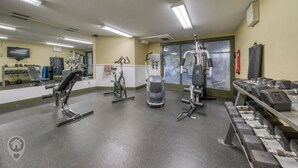 Una palestra con diverse attrezzature per esercizi, un televisore e uno specchio.