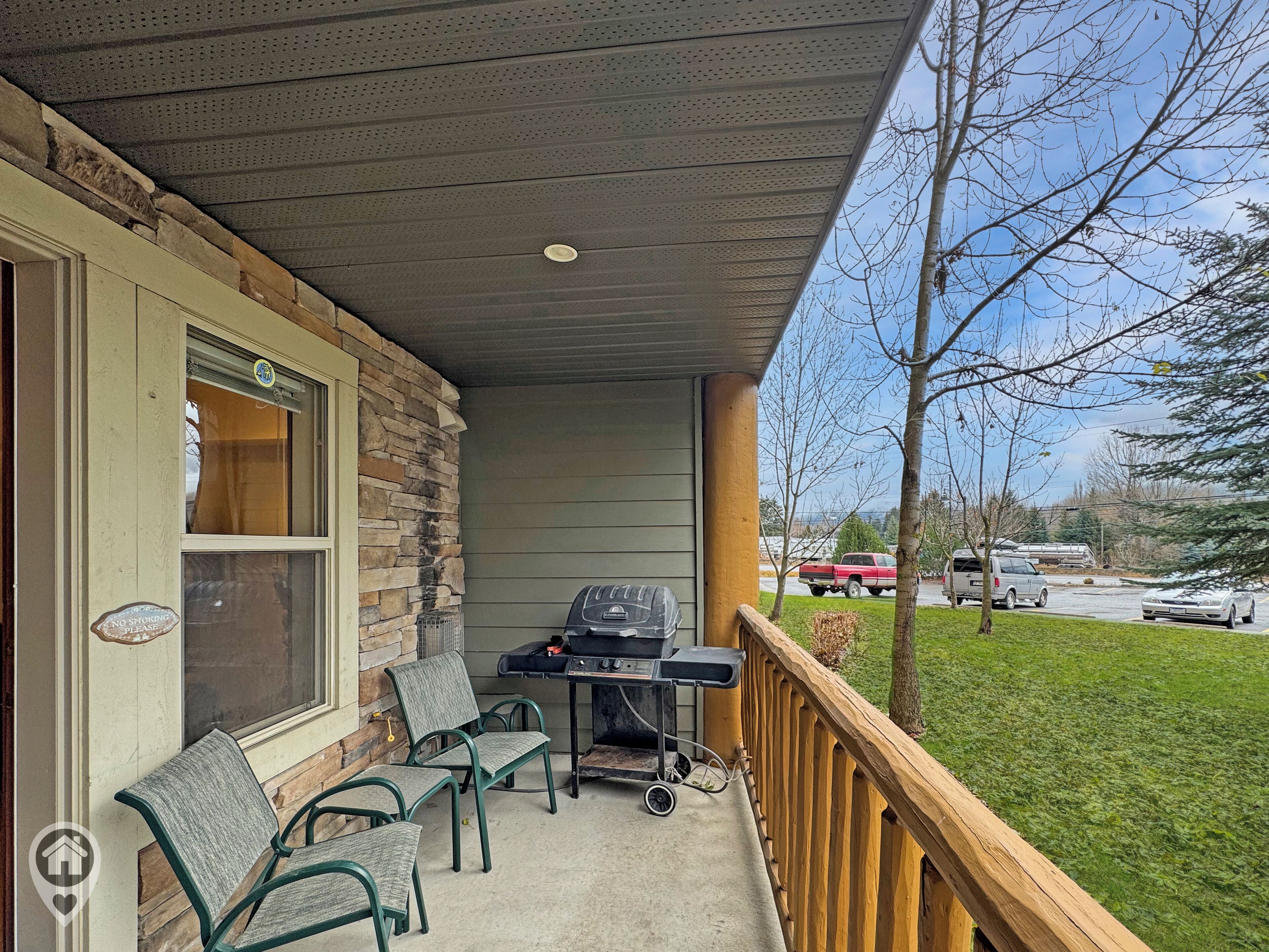 A covered porch with a grill, chairs, and a view of a parking lot.