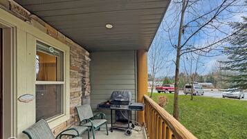 A covered porch with a grill, chairs, and a view of a parking lot.