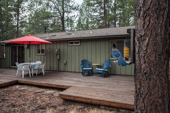 A wooden deck with outdoor furniture, a red umbrella, and a bird feeder. - Cozy Sunriver Analog Escape (Sunriver)