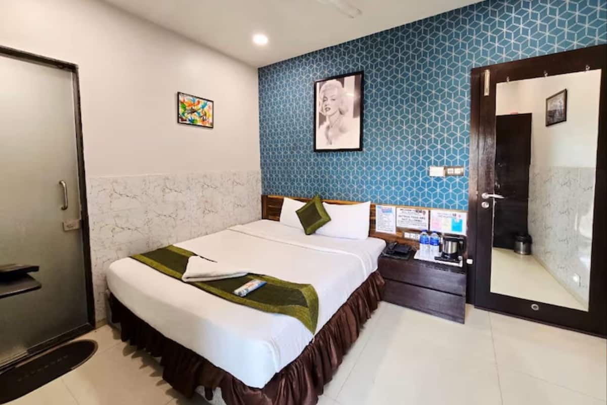 A hotel room with a bed, a desk, a mirror, and a door.