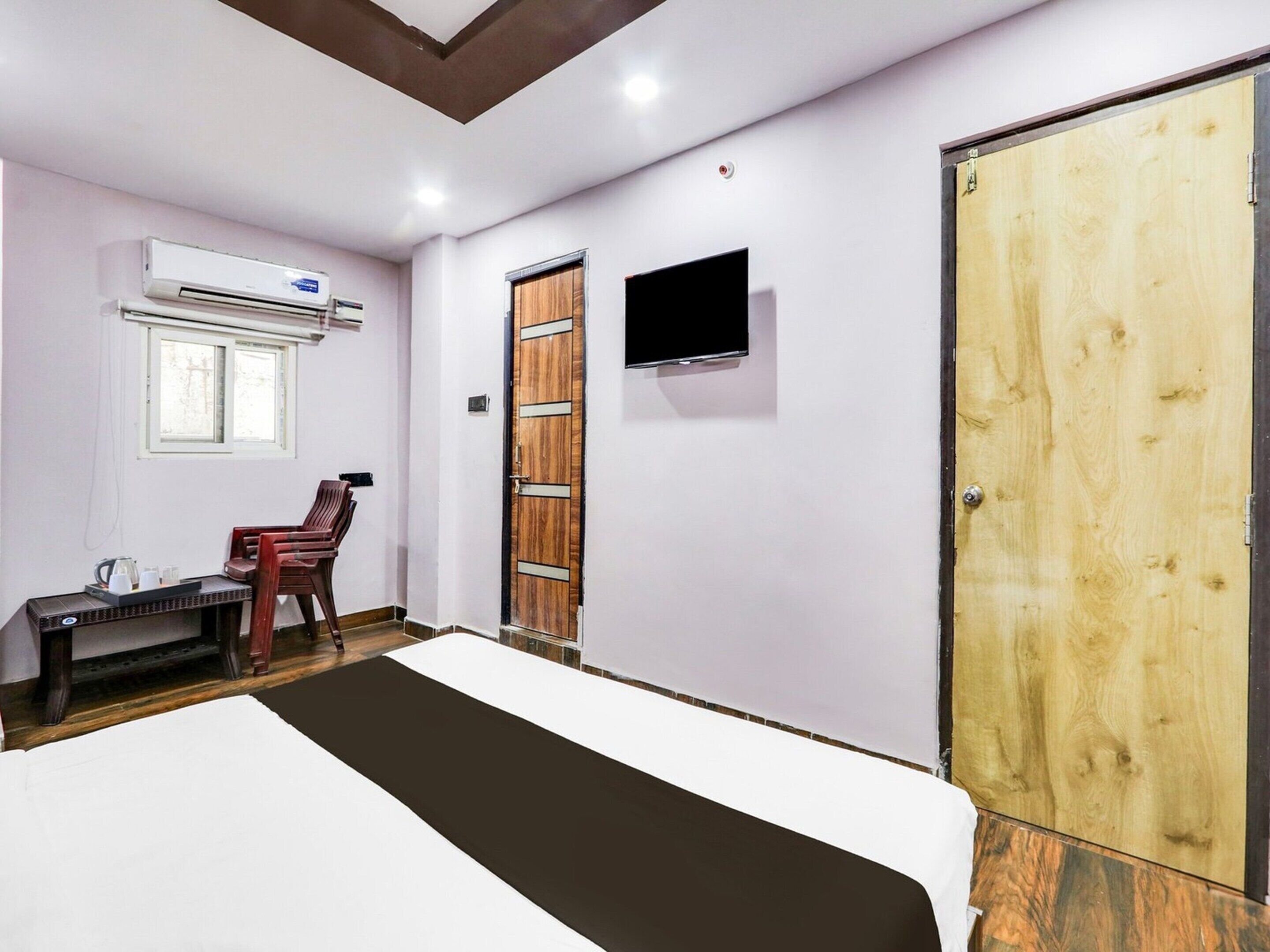 Una habitación con una cama, un escritorio con silla, un aire acondicionado, un televisor y una puerta de madera.