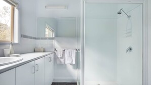 A modern bathroom with a glass shower enclosure, a sink with a mirror above it, and a window providing natural light. - Secluded Grampians Cottage with Mountain Views & Wildlife (Dunkeld)