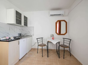 A compact kitchen with a marble countertop, white cabinets, and a small dining area with two chairs and a table. - Calm and Stylish Rooms With Balcony - Studio Apartment With Balcony (Rovinj)
