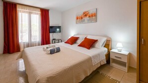 Une chambre d’hôtel avec un grand lit, des rideaux rouges, un téléviseur à écran plat, un tableau au mur et une table de chevet avec une lampe.
