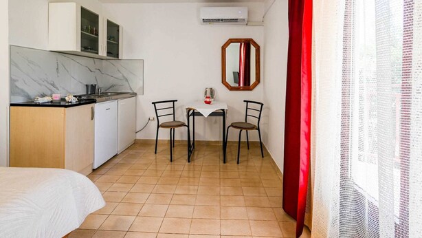 Une chambre d’hôtel compacte comprenant un coin cuisine, une petite table à manger avec deux chaises, un lit et un miroir au mur.