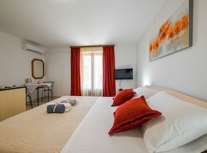 A hotel room with a bed, a desk, a chair, a TV, and a painting on the wall. - Calm and Stylish Rooms With Balcony - Studio Apartment With Balcony (Rovinj)