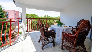 Un balcon avec des fauteuils et une table en osier, donnant sur un jardin et des immeubles.