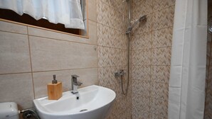 Une salle de bain avec un lavabo blanc, une douche et un miroir sur lequel est accrochée une serviette.