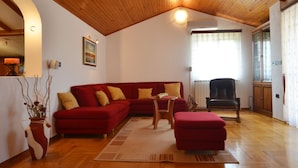 A living room with a wooden ceiling, a red sofa, a small table, and a black chair. - Green Oasis Family Getaway (Rovinj)