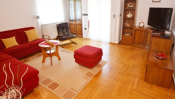 A living room with a red sofa, a red ottoman, a wooden coffee table, a leather chair, a television, and a cabinet. - Green Oasis Family Getaway (Rovinj)