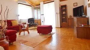 A cozy living room with a wooden ceiling, red furniture, a television, and a bookshelf. - Green Oasis Family Getaway (Rovinj)