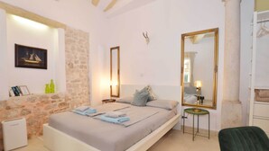 Une chambre à coucher avec un lit, une table de chevet, un miroir et un mur en pierre.