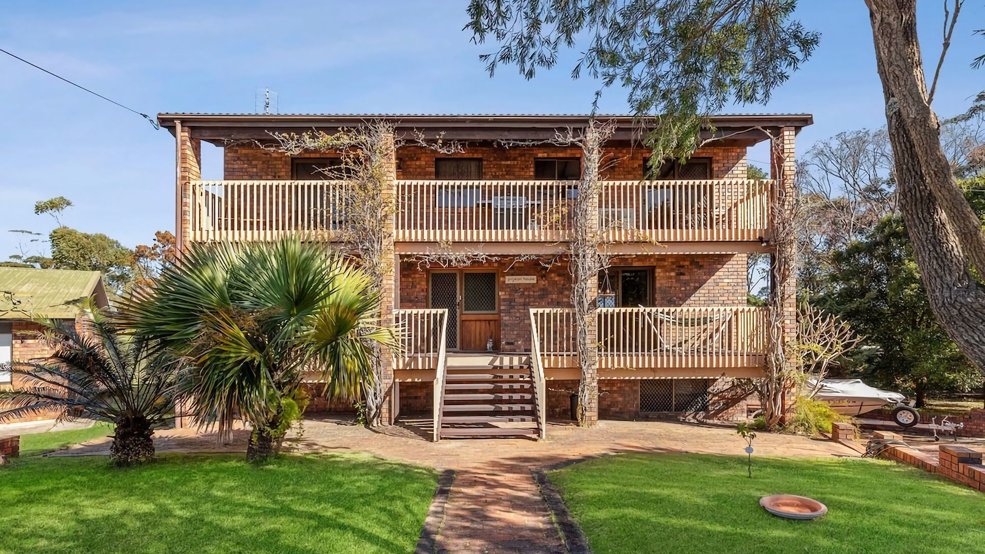 A two-story building with a balcony on the upper floor, a front door, and a small garden area with a palm tree.