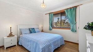 Ein Schlafzimmer mit Bett, Nachttischen, einem Fenster mit Vorhängen, einer Pendelleuchte und einer Topfpflanze.