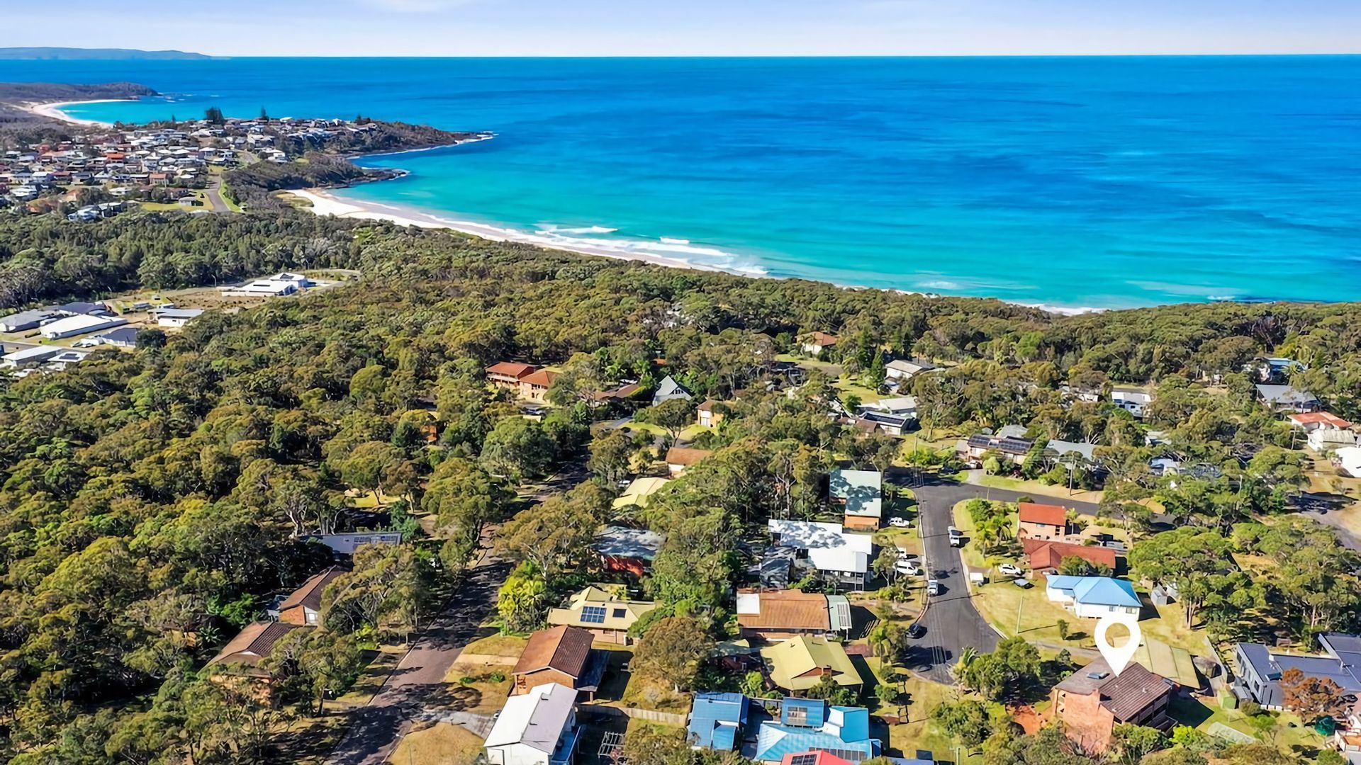 Vista aérea de una zona residencial costera con casas, caminos y una playa.