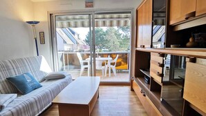 Een moderne woonkamer met een bank, een salontafel en een eethoek met stoelen. Er is een schuifdeur naar een balkon met uitzicht op gebouwen en bomen.