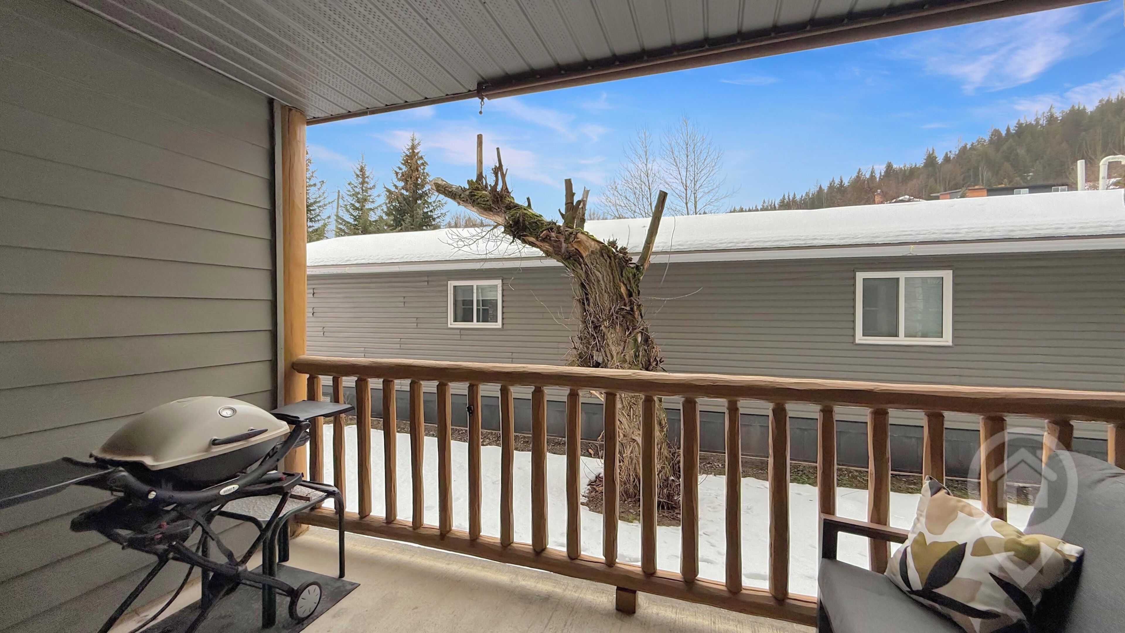 A balcony with a wooden railing, a barbecue grill, and a view of a house with a tree in the background.
