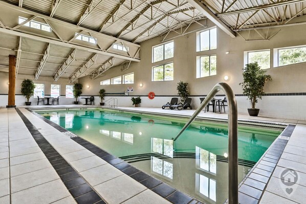 An indoor swimming pool with clear water, surrounded by tiled flooring and potted plants.