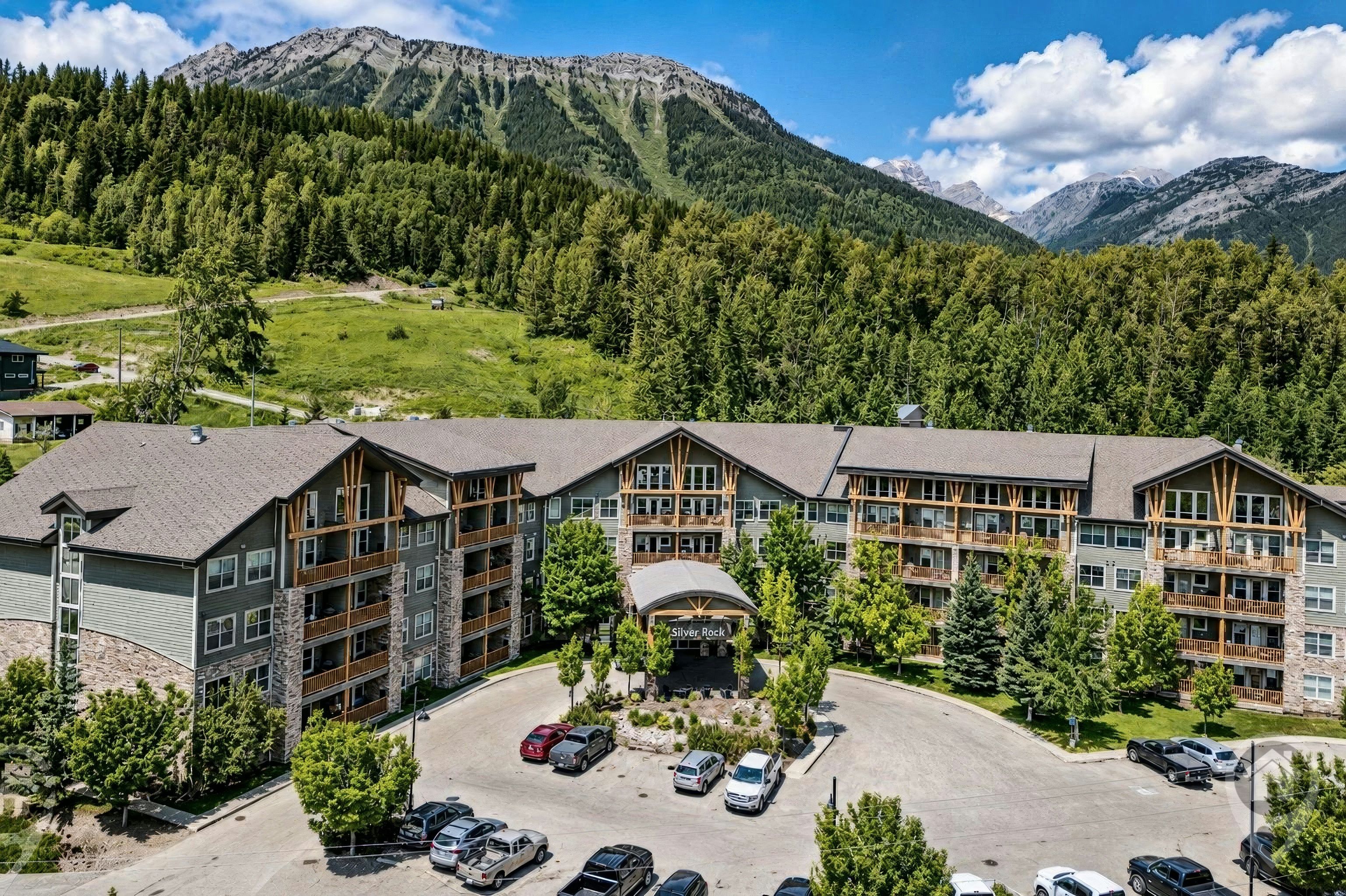Ein mehrstöckiges Hotel mit Parkplatz, umgeben von bewaldeten Hügeln und Bergen.