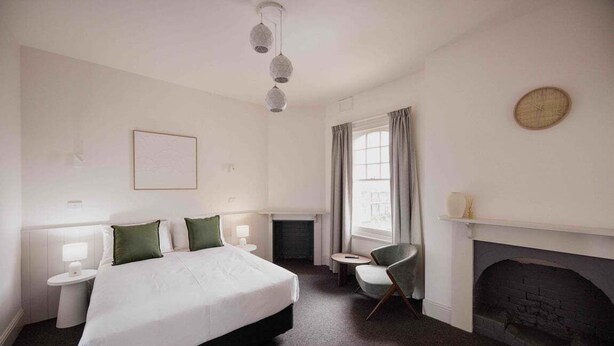 Quarto de hotel com uma cama grande, lareira, uma mesa redonda pequena e uma cadeira.