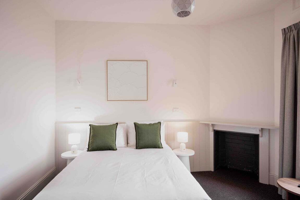 Quarto de hotel com uma cama grande, duas mesas de cabeceira com luminárias, uma lareira e um quadro emoldurado na parede.