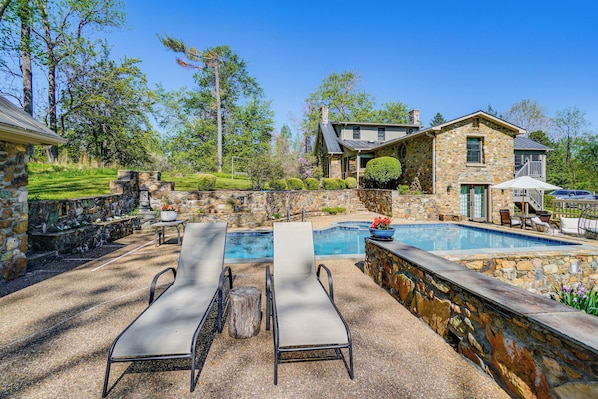 Una casa de piedra con piscina, sillas de descanso y un muro de piedra.