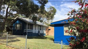 A two-story house with a blue exterior, a fenced yard, and a tree in the background. - Sting Ray Bay near Boat Harbour Beach (Bendalong)