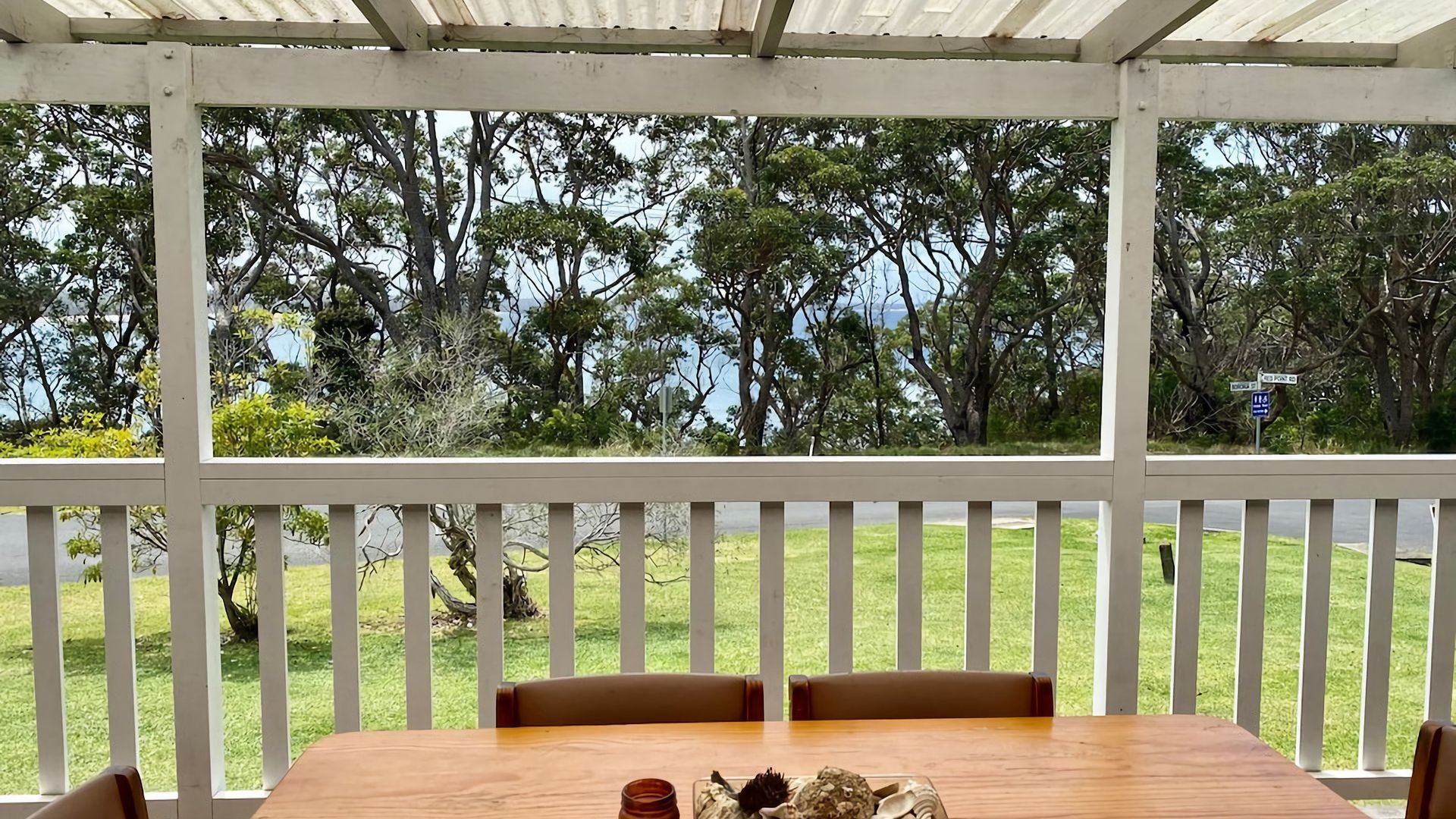 A covered outdoor seating area with a table and chairs, overlooking a grassy landscape and trees.