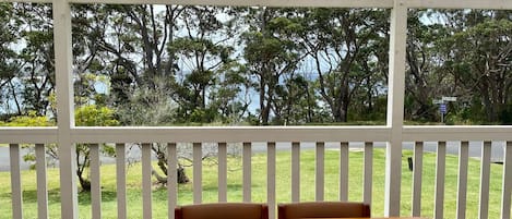 Un espace extérieur abrité, avec une table et des chaises, donnant sur un paysage verdoyant et des arbres.