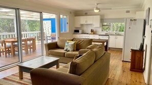 A cozy living room with a sofa and a coffee table, a dining area with wooden furniture, and a kitchen with white cabinets and a refrigerator. - Sting Ray Bay near Boat Harbour Beach (Bendalong)