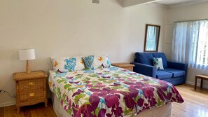 A bedroom with a bed, a nightstand, a blue sofa, and a window with curtains. - Sting Ray Bay near Boat Harbour Beach (Bendalong)