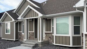 A modern two-story house with a stone foundation, grey siding, and a large bay window.